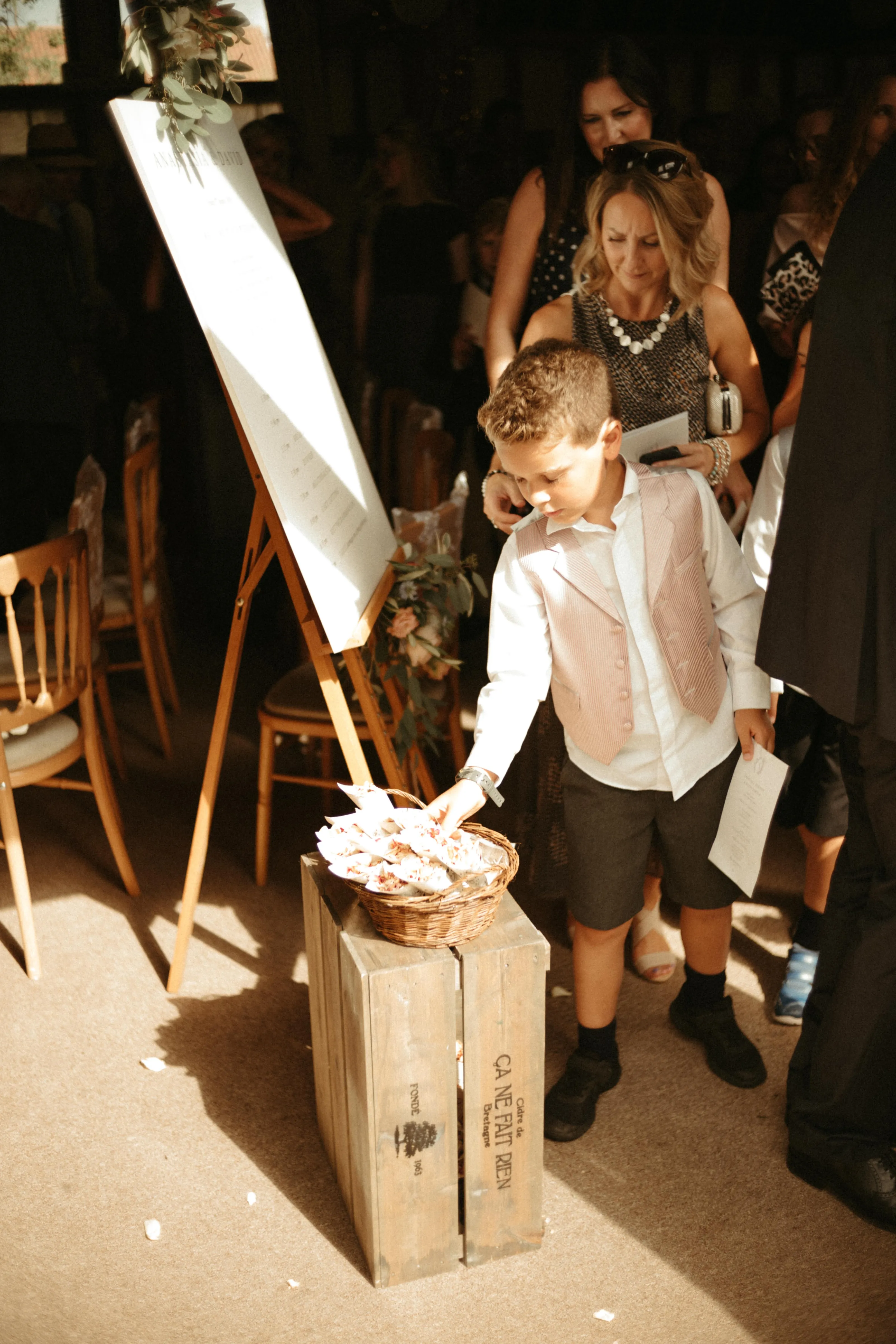 Boy in waistcoat collects confetti from basket at wedding.