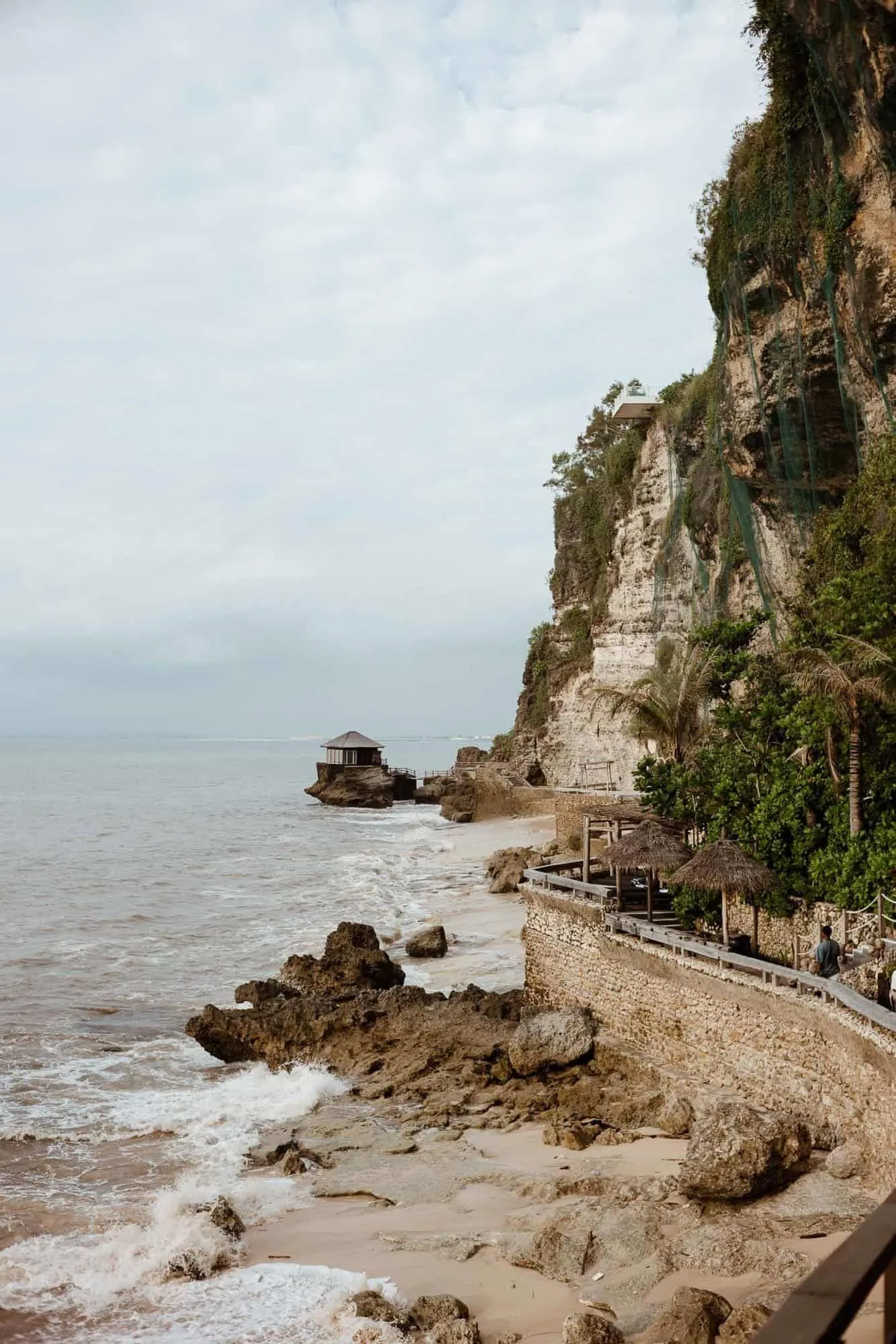 Coastal scene with rocky beach, cliff, and building on a sea rock.