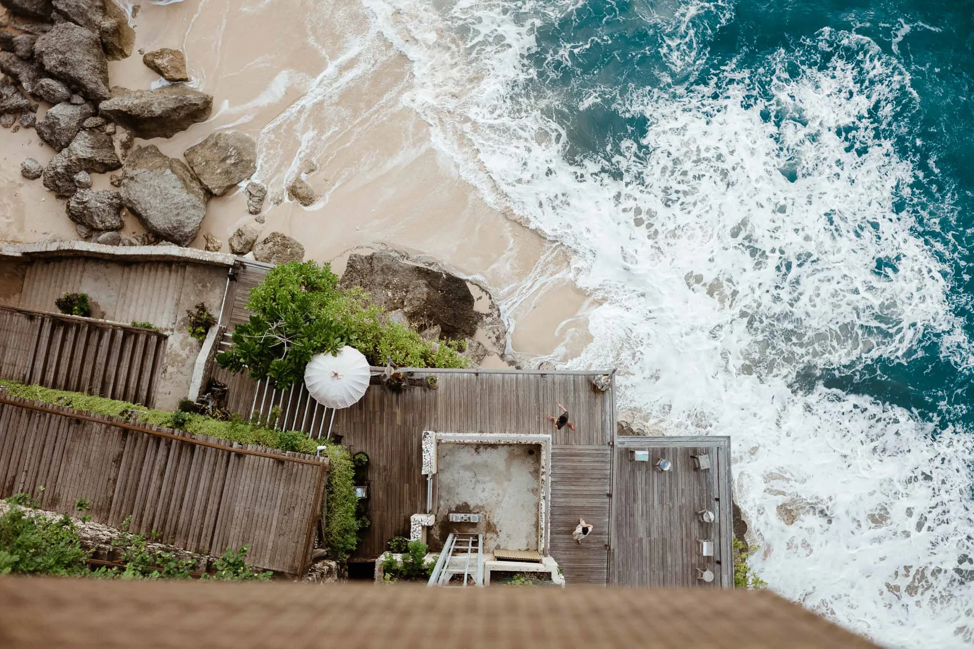 Overhead view of beach, ocean waves, and cliffside wooden decks with people.
