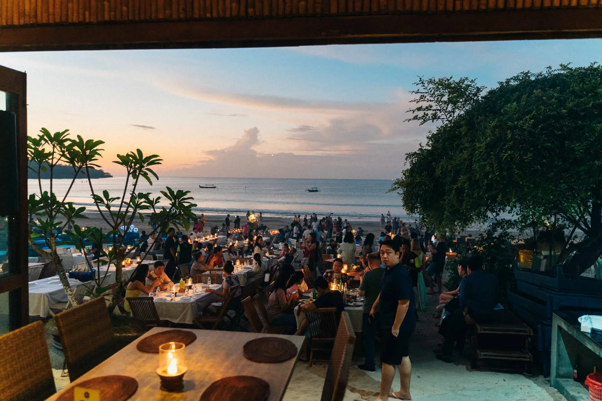 People dining on a beach at sunset with ocean view.