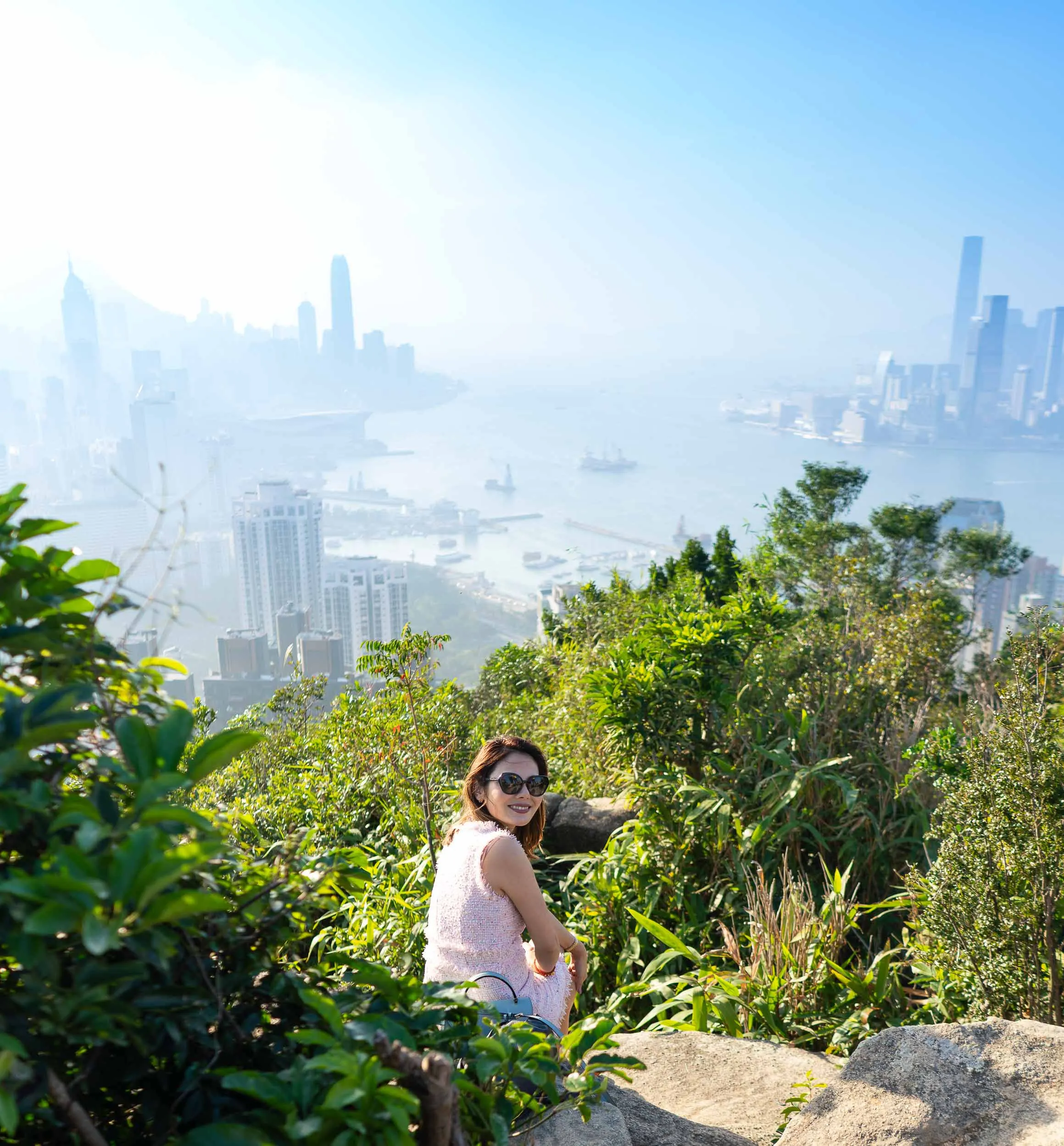 Smiling woman in pink dress on a hill, city skyline and harbour behind.