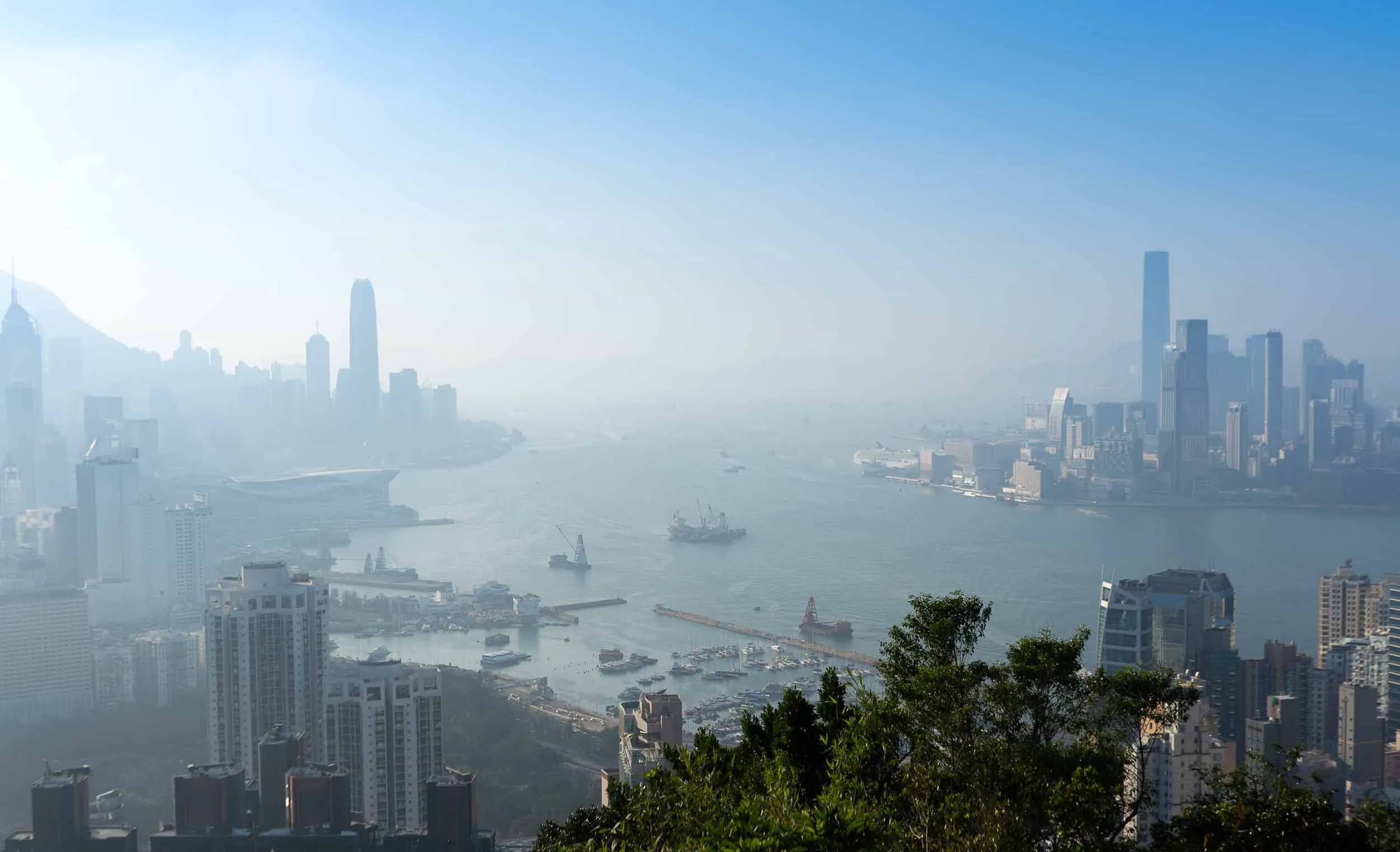 Hazy Hong Kong skyline and Victoria Harbour with many boats.