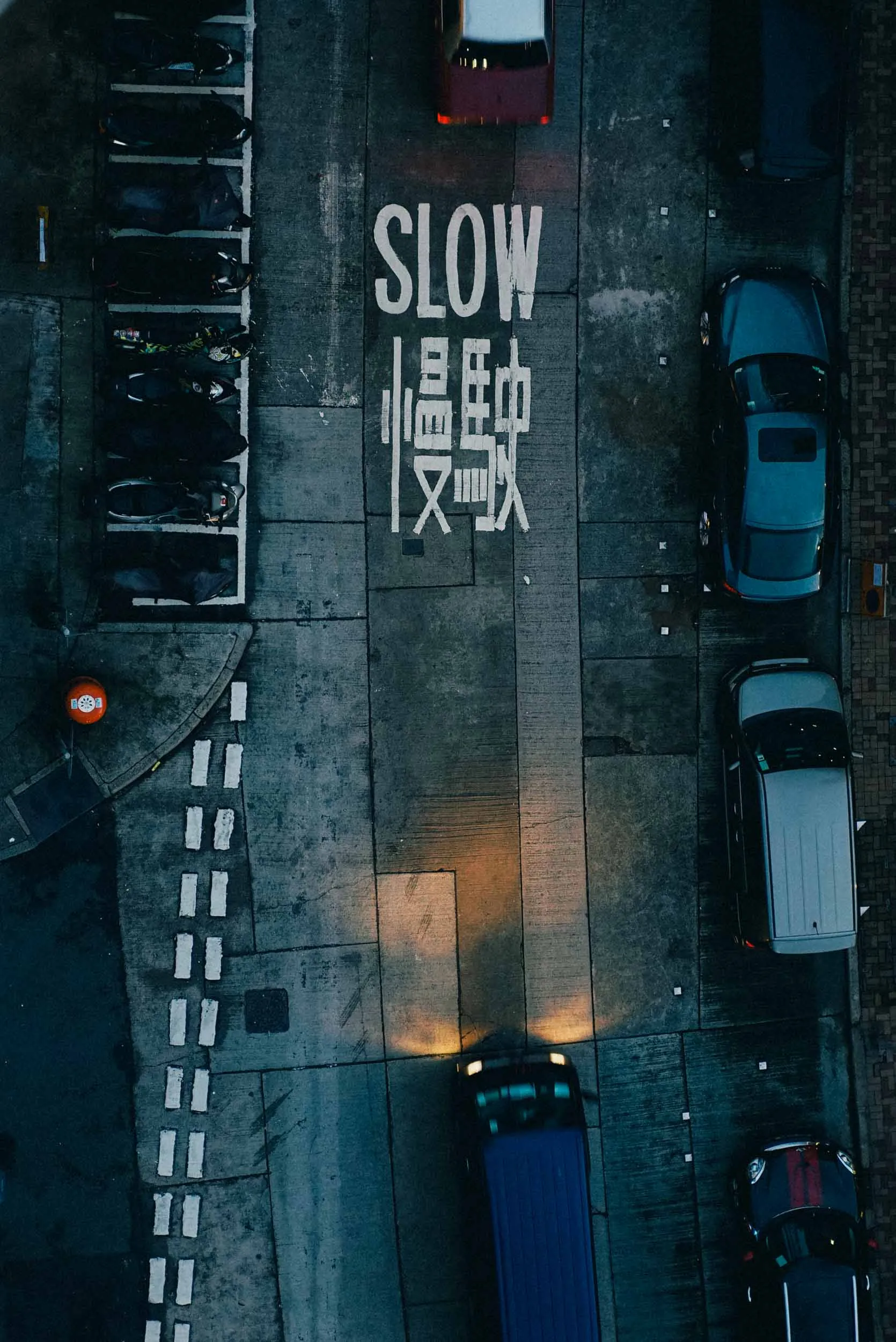 Overhead street view with "SLOW" and Chinese characters, cars, motorbikes, and headlights.