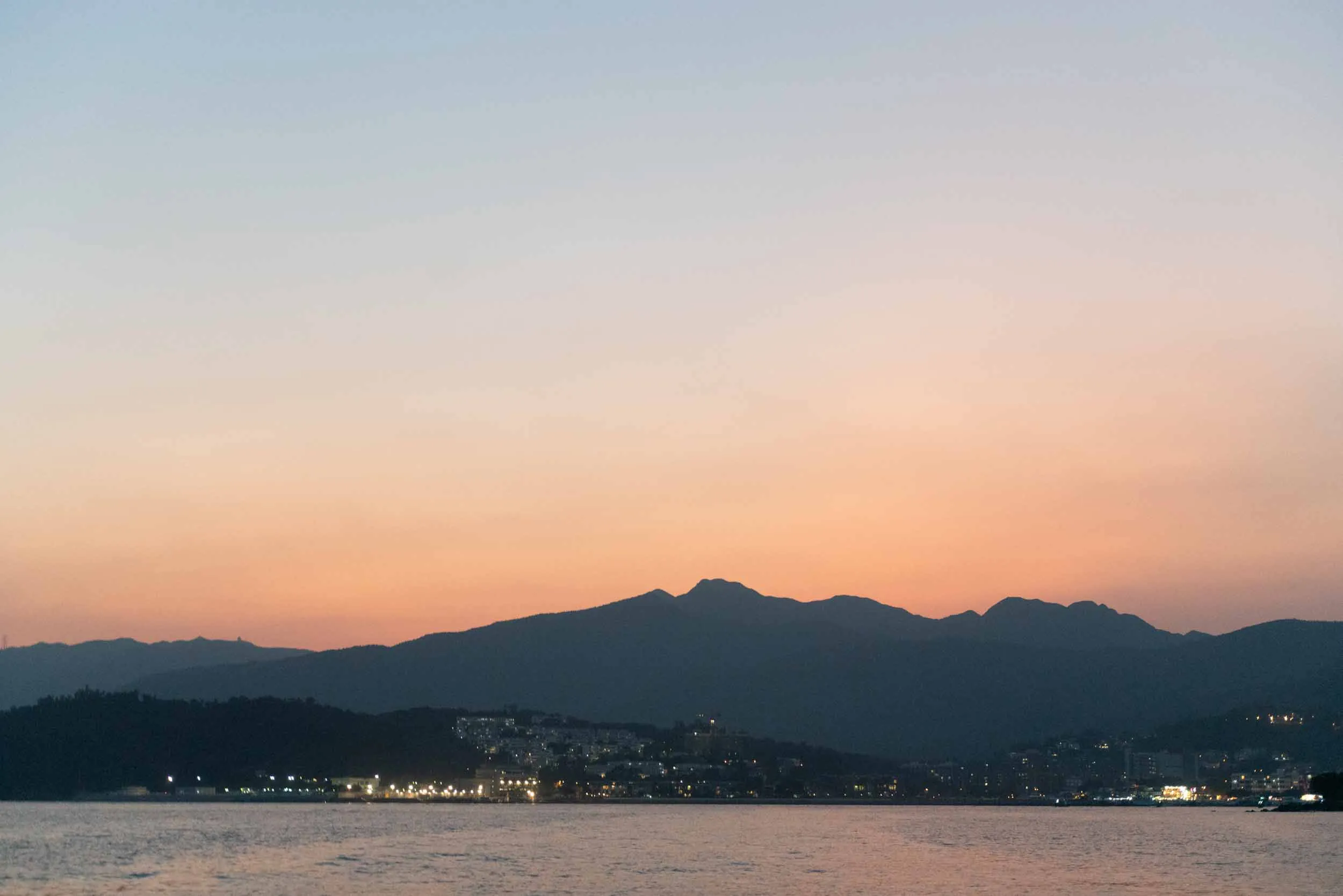 Dusk over mountains and a coastal town with lights by the sea.