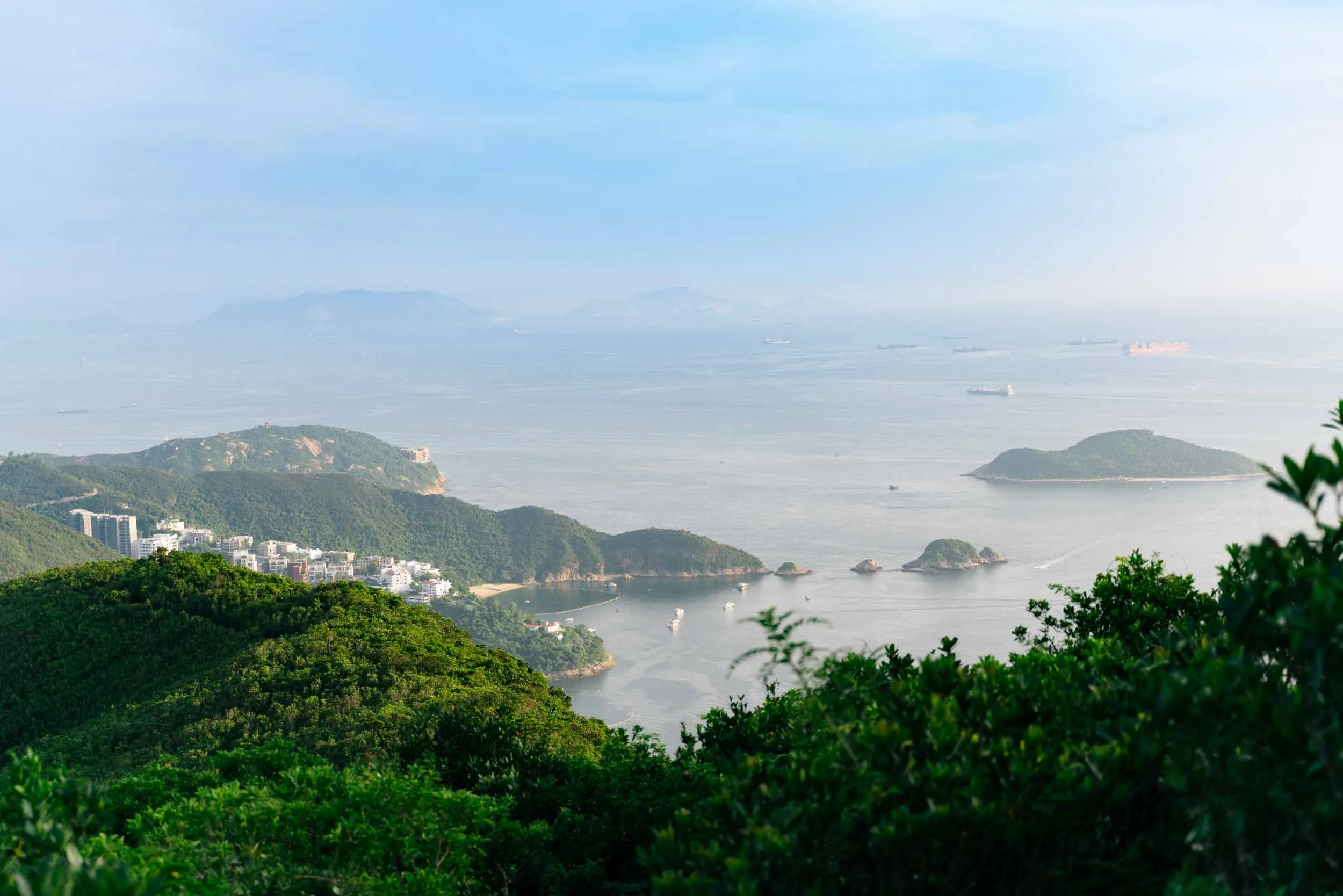 Aerial view of green hills, a coastal town, small islands, and ships on the sea.