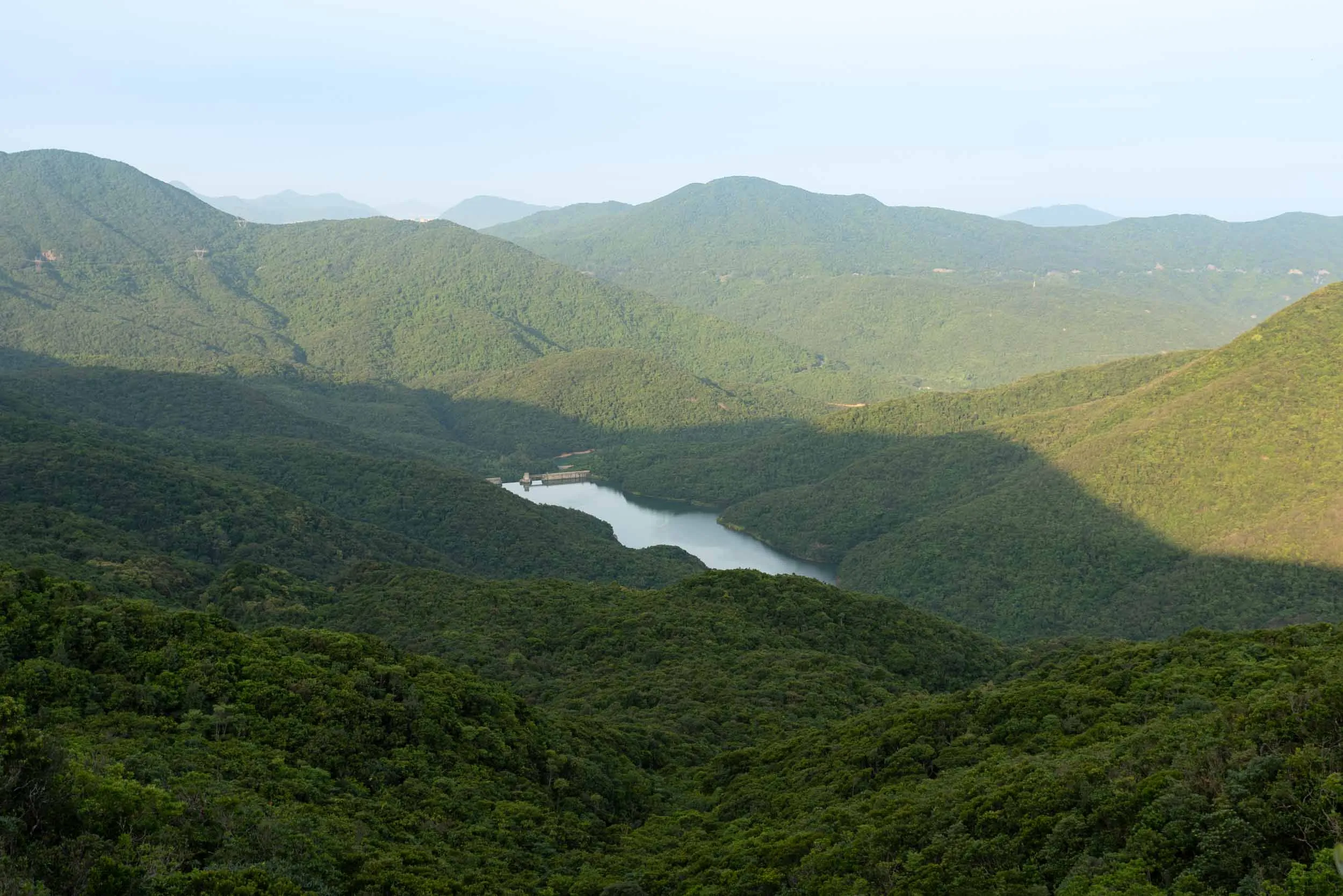 Green, forested hills surround a reservoir with a visible dam.