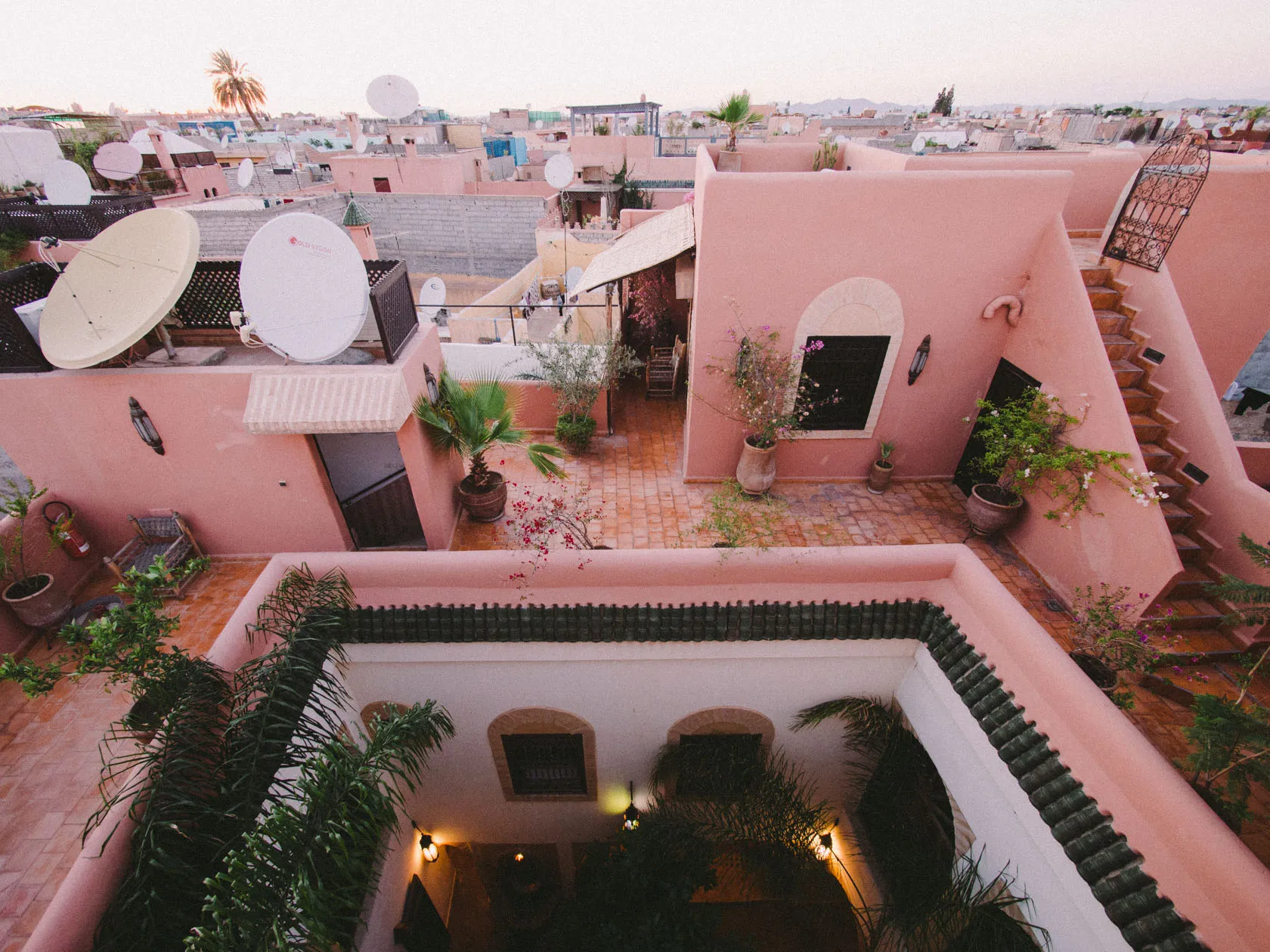 Pink city rooftops with satellite dishes, potted plants, and an open courtyard.