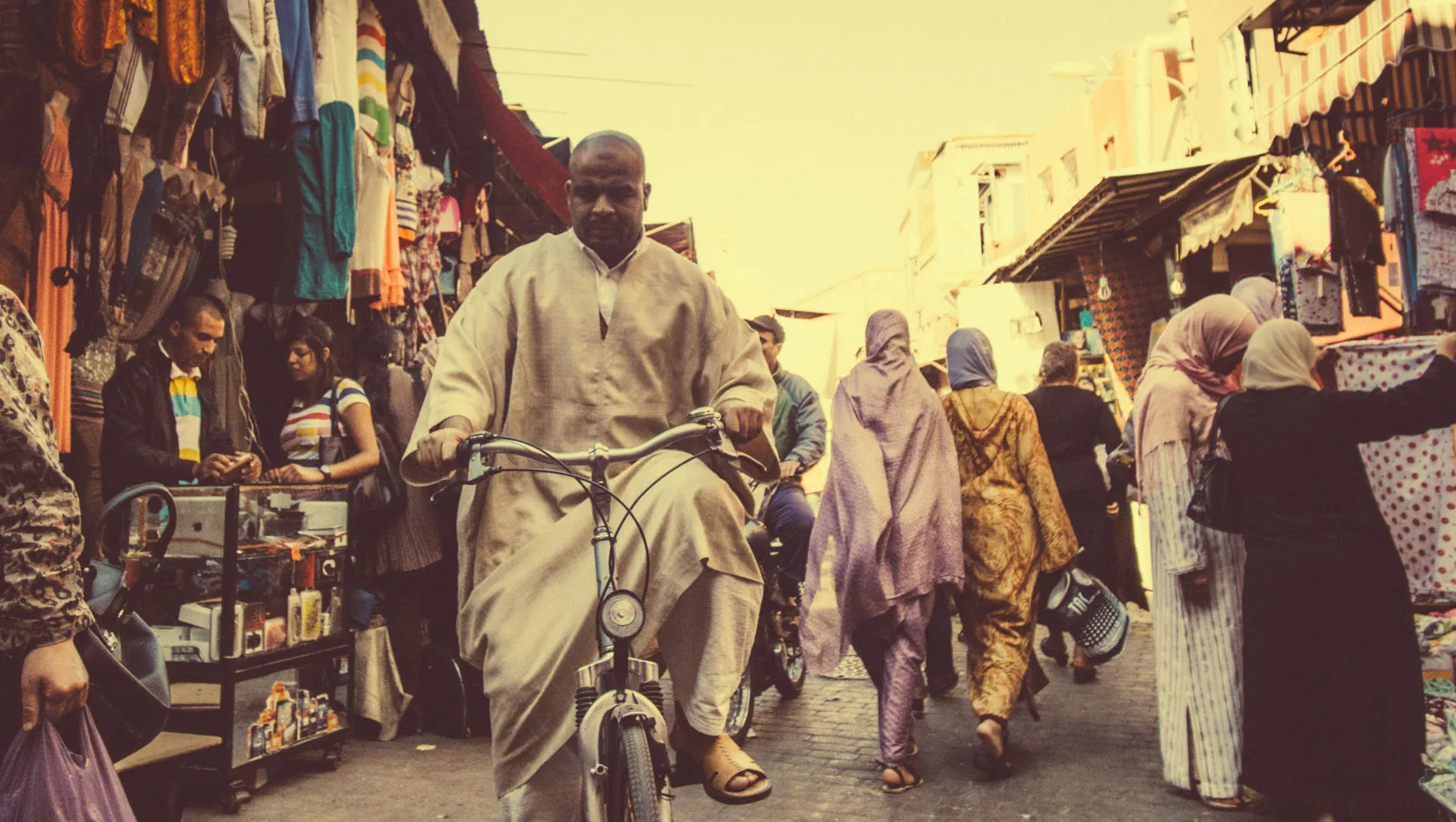 Man cycling through a busy market street with people and stalls.