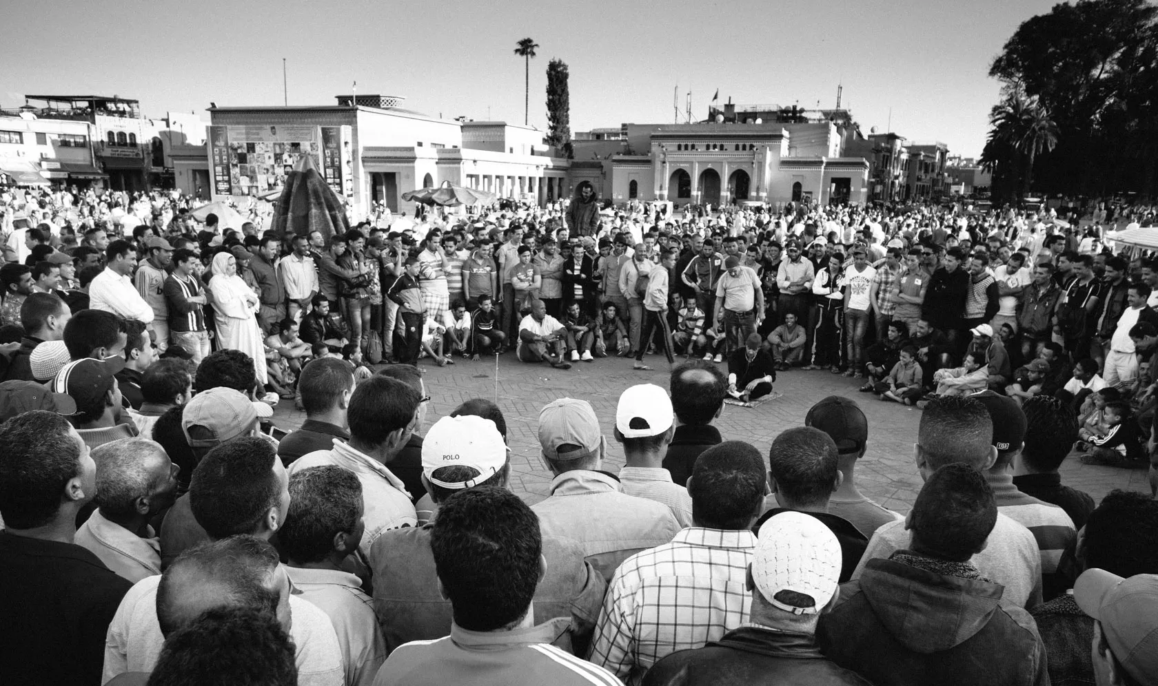 Black and white crowd watching a street performer in a square.