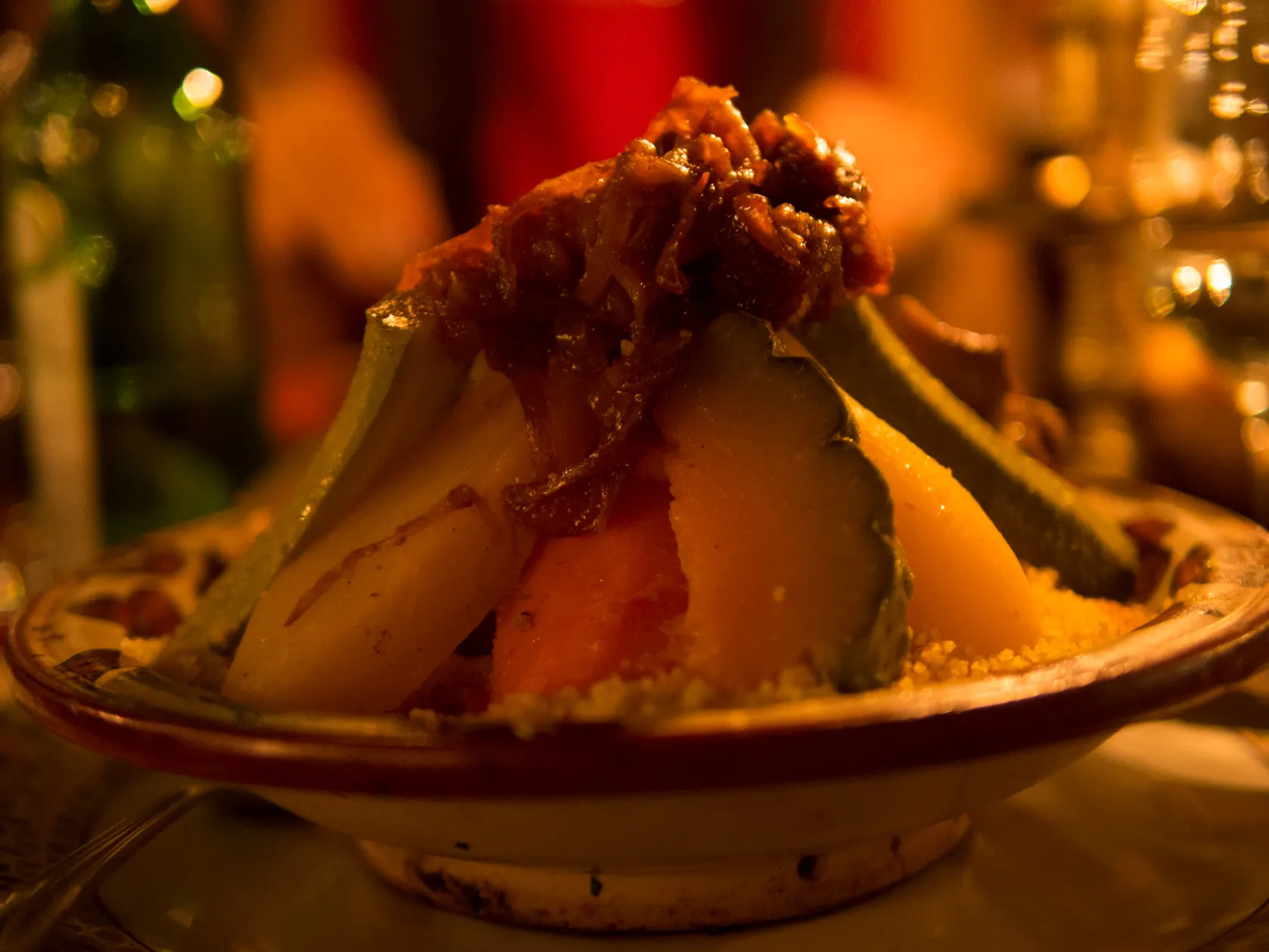Warmly lit couscous, vegetables, and stewed meat in a patterned bowl.