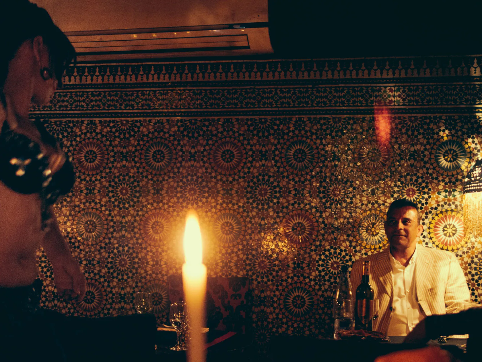 Man and woman at a candlelit table, intricate patterned wall.