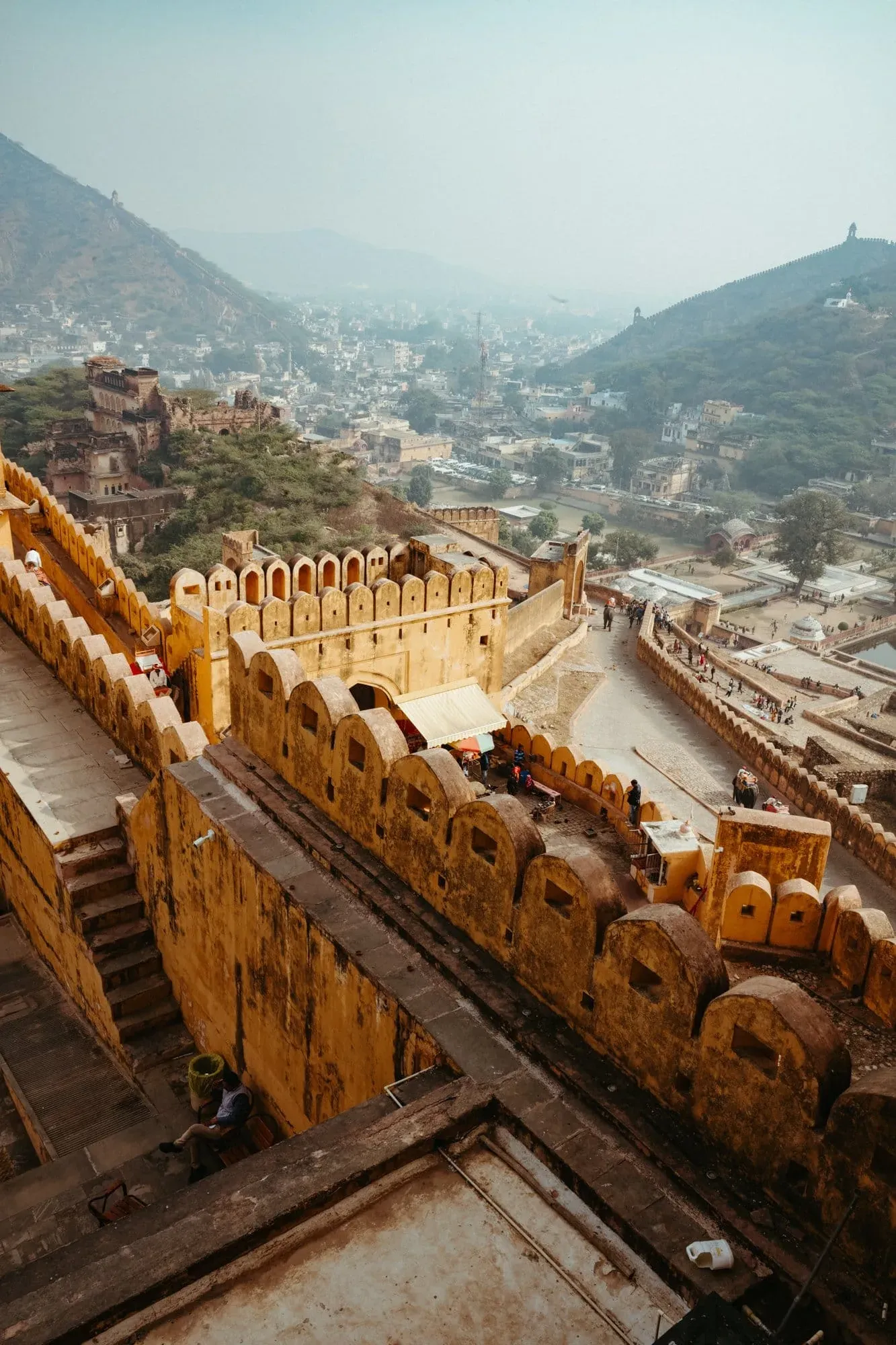 A vertical view over the ochre ramparts of Amber Fort towards a hazy Jaipur valley.