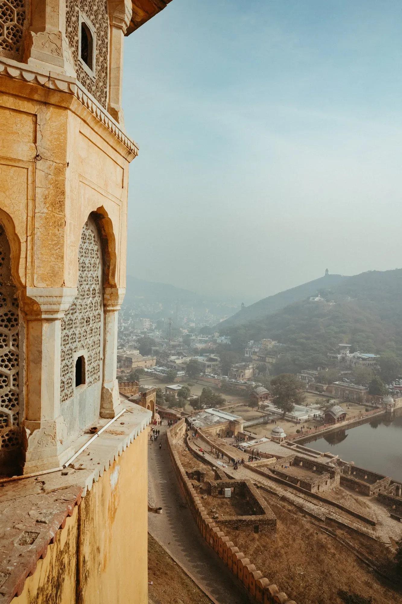 An ochre tower of Amber Fort overlooking its ramparts, Maota Lake and the hazy Jaipur hills.