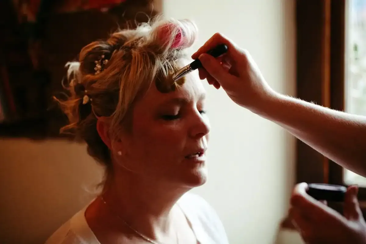 Woman with hair curlers having makeup applied to her forehead.