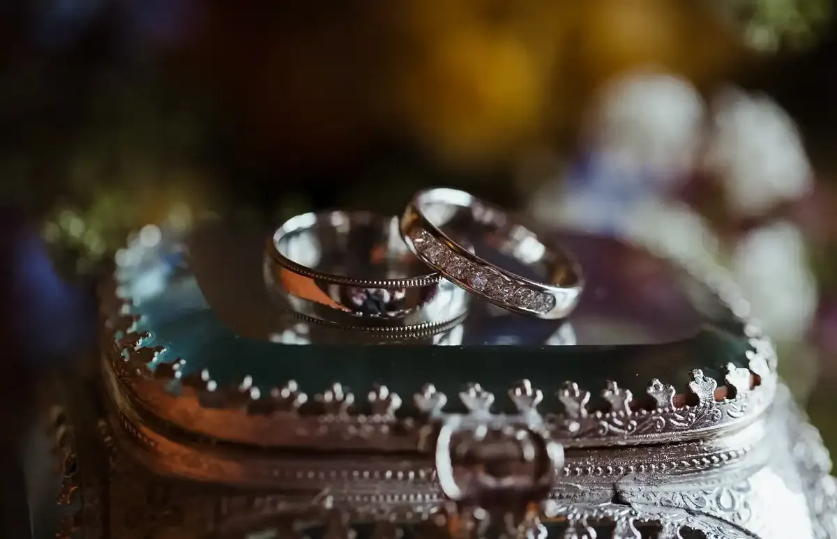 Two silver wedding rings, one with diamonds, on an ornate silver box.