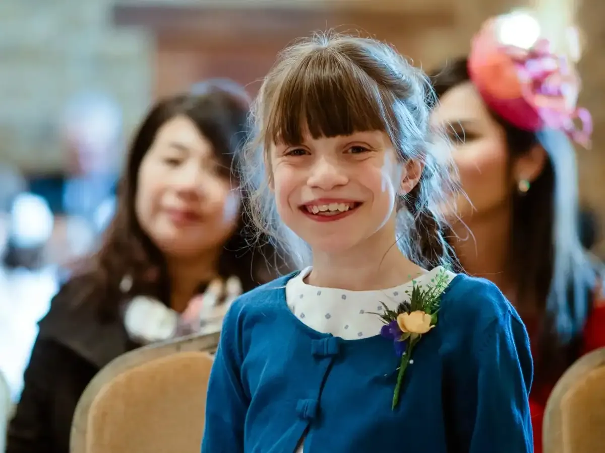Smiling girl in blue cardigan with a small floral pin.