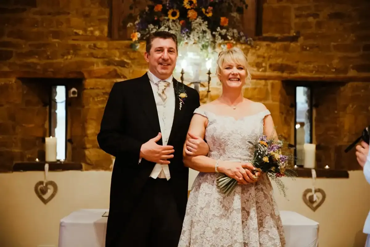 Smiling bride and groom in wedding outfits, holding a wildflower bouquet.