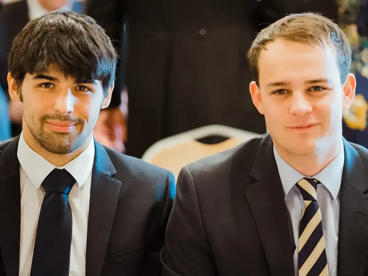 Two smiling men in dark suits, one with a striped tie.