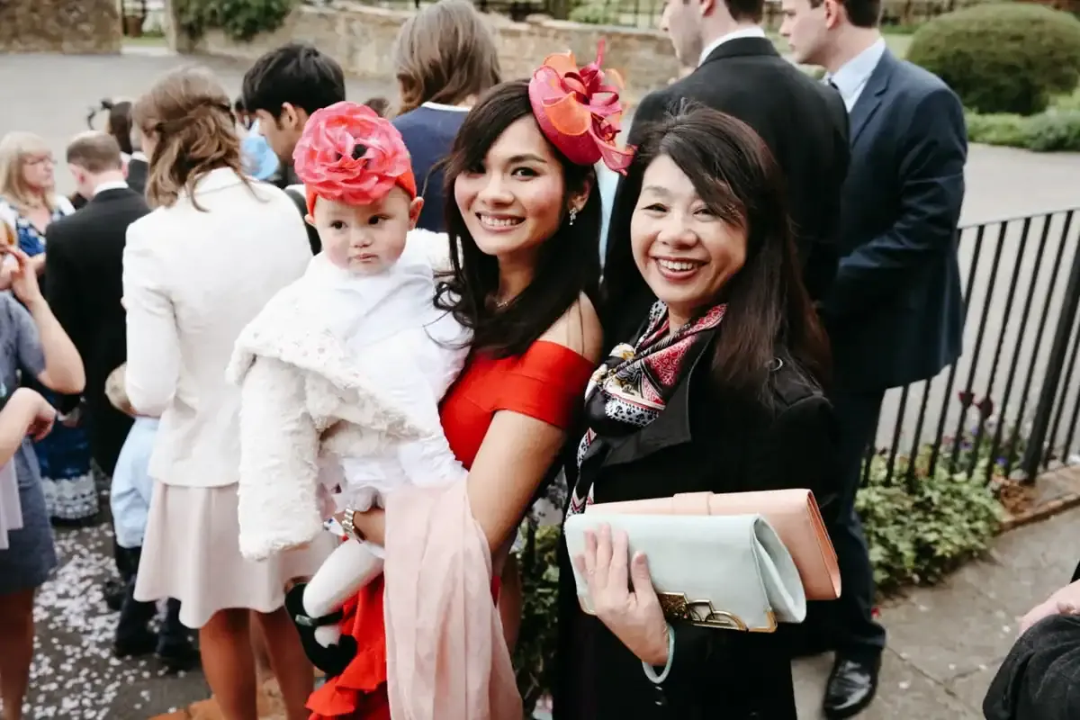 Three smiling women, one holding a baby with a pink flower headband.