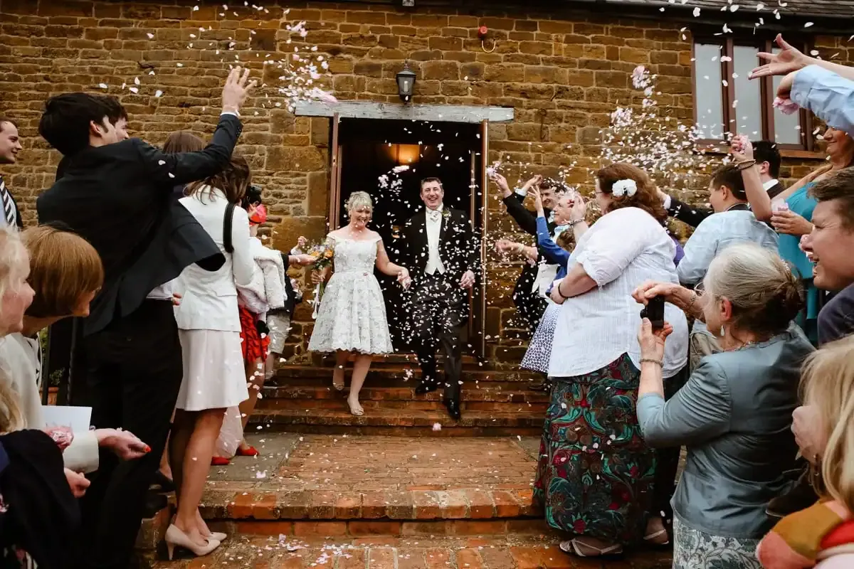 Guests throw confetti over a newlywed couple descending steps.