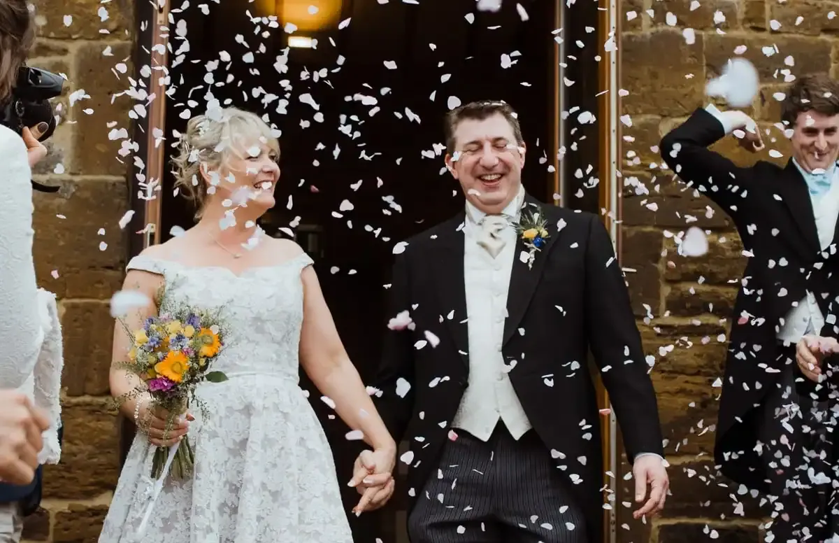 Smiling bride and groom holding hands, showered with confetti.