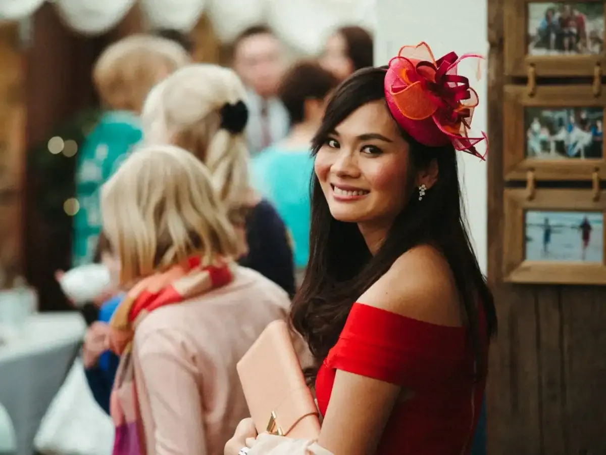 Smiling woman wearing a red dress and a pink fascinator.