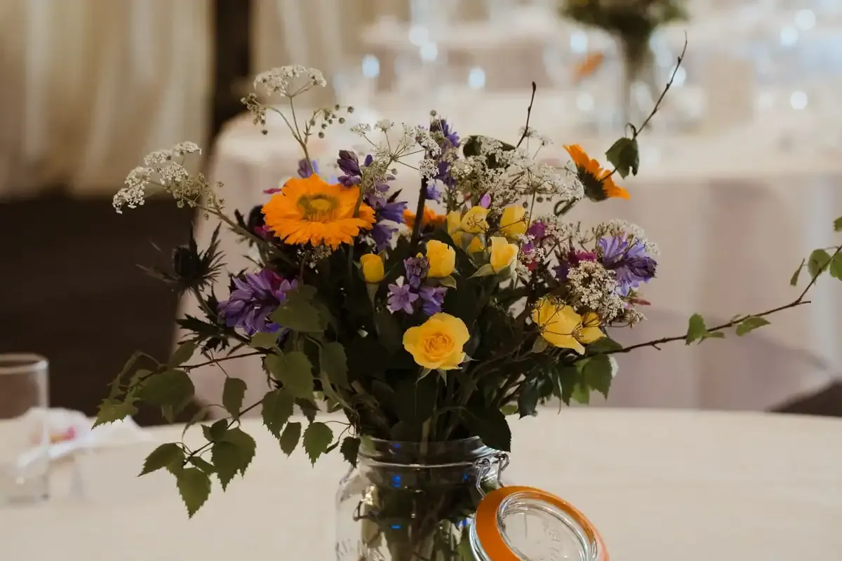 Bouquet of orange, yellow, and purple flowers in a glass jar.