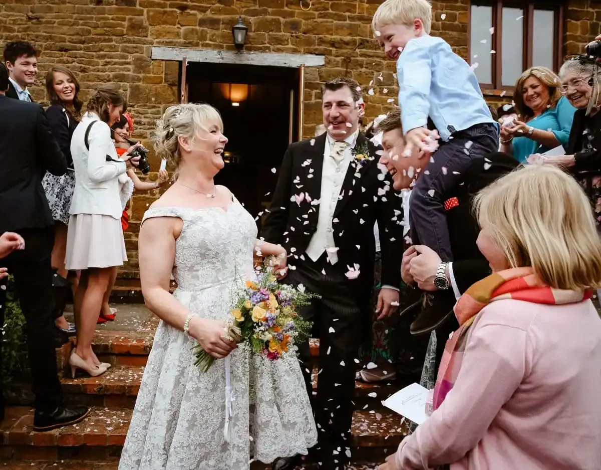 Happy bride, groom, and guests showered with confetti outside a stone building.