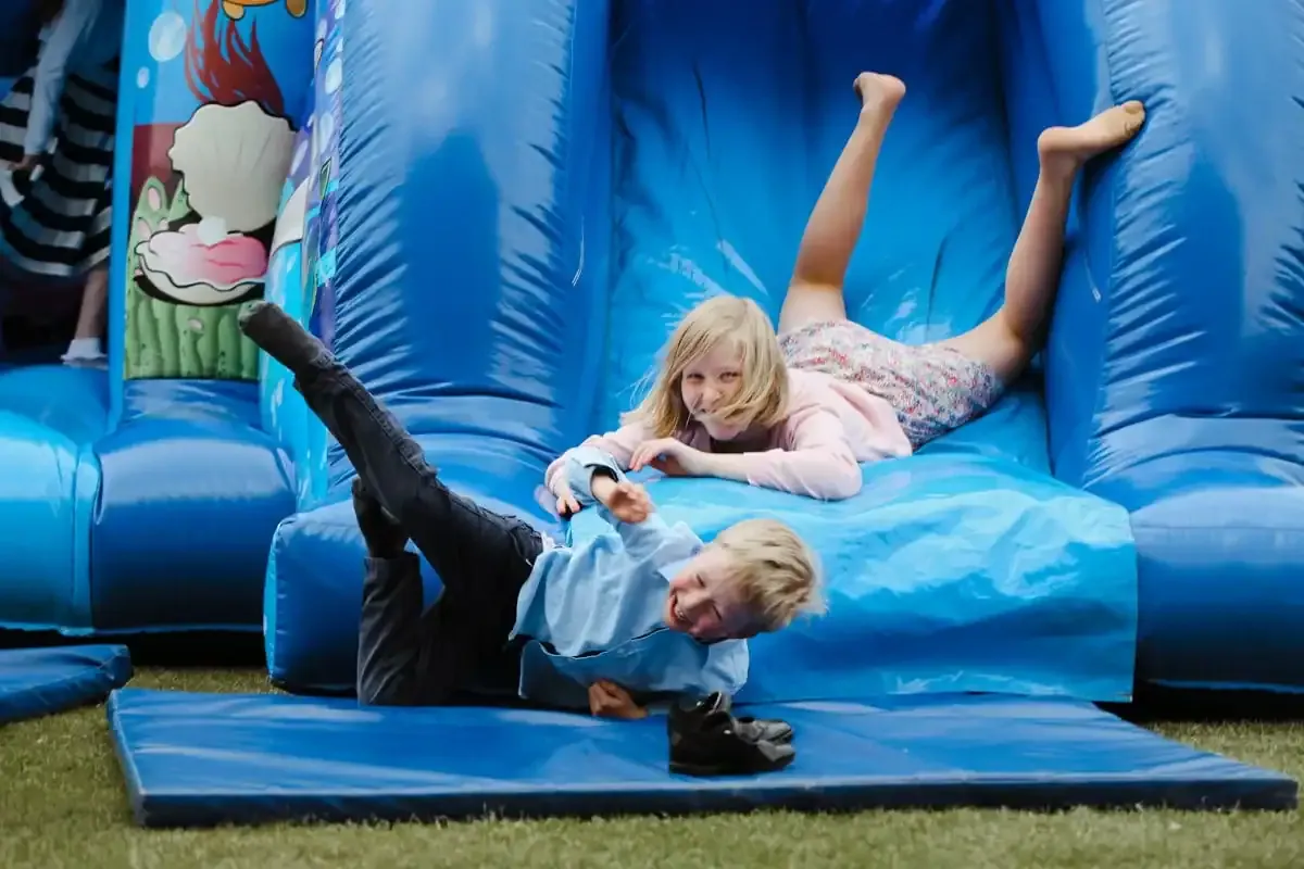 Two children laughing on a blue inflatable bouncy castle.