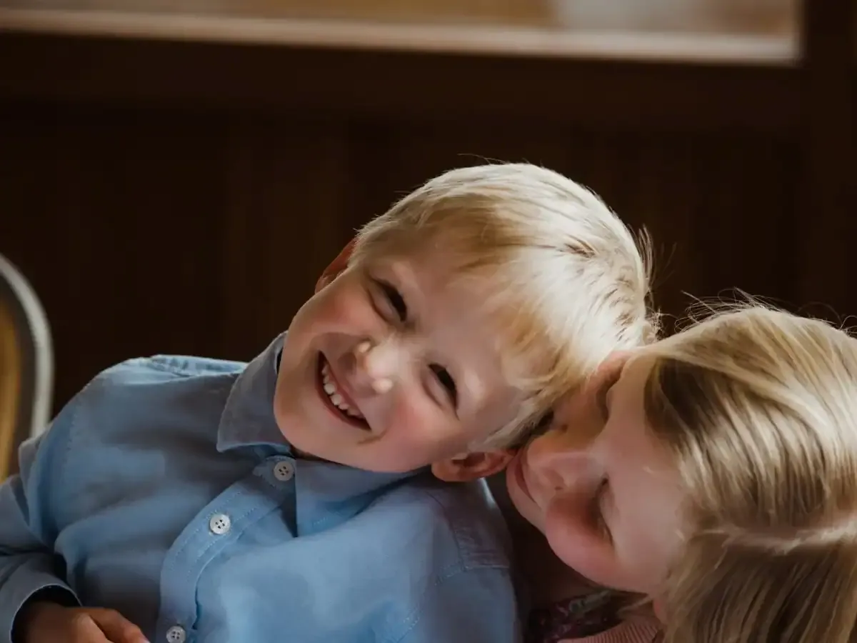 Blonde boy smiling with closed eyes, girl leaning affectionately on his shoulder.