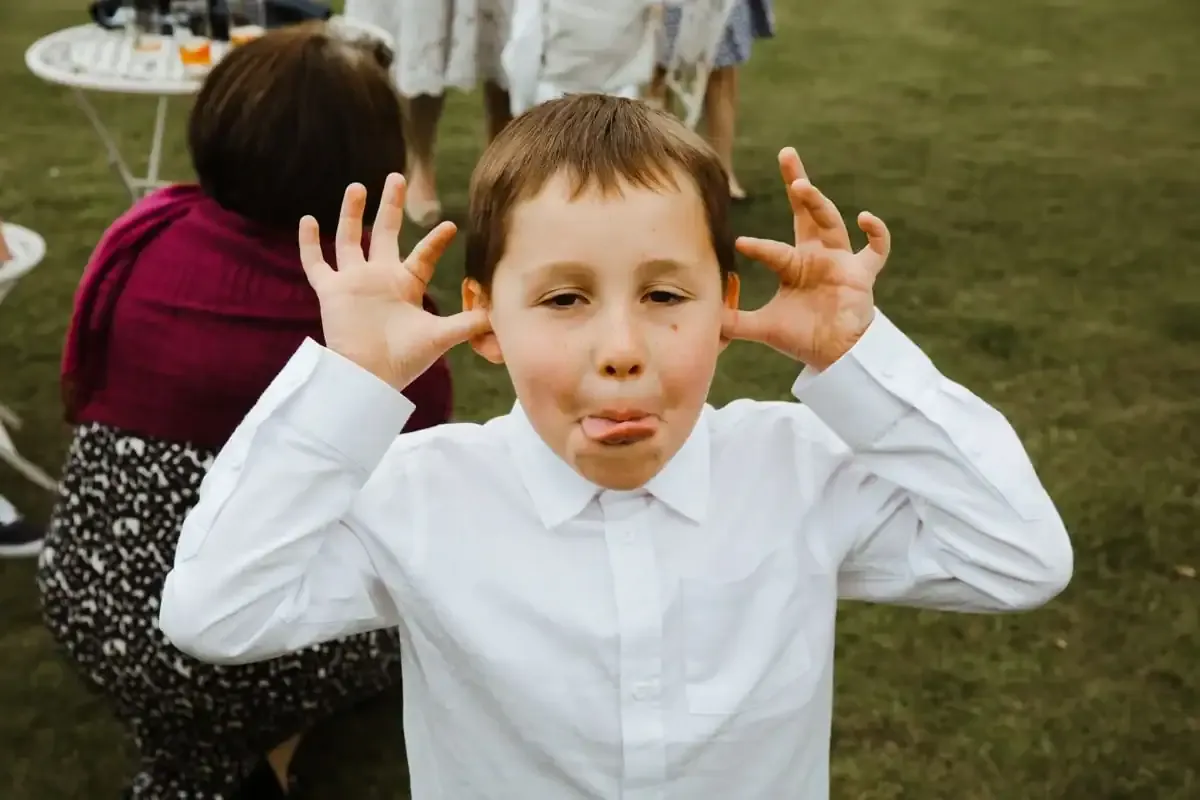 Boy in white shirt pulling ears and sticking out tongue, making a funny face.