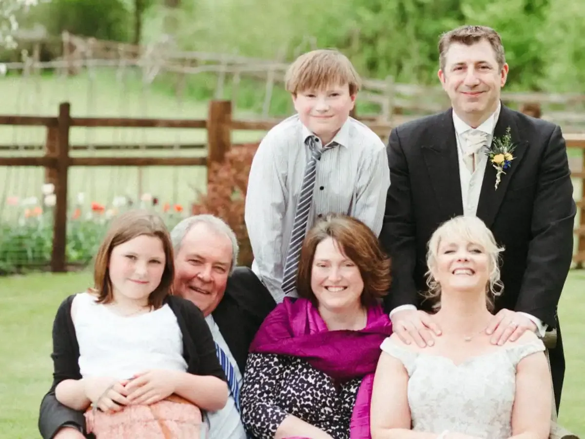 A smiling family of six, including a bride, groom, and children, outdoors.