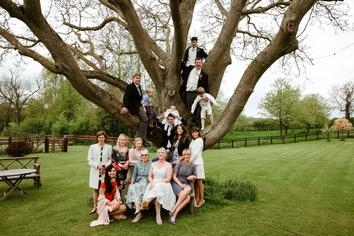 Large group of adults and children posing on grass and in a huge tree.