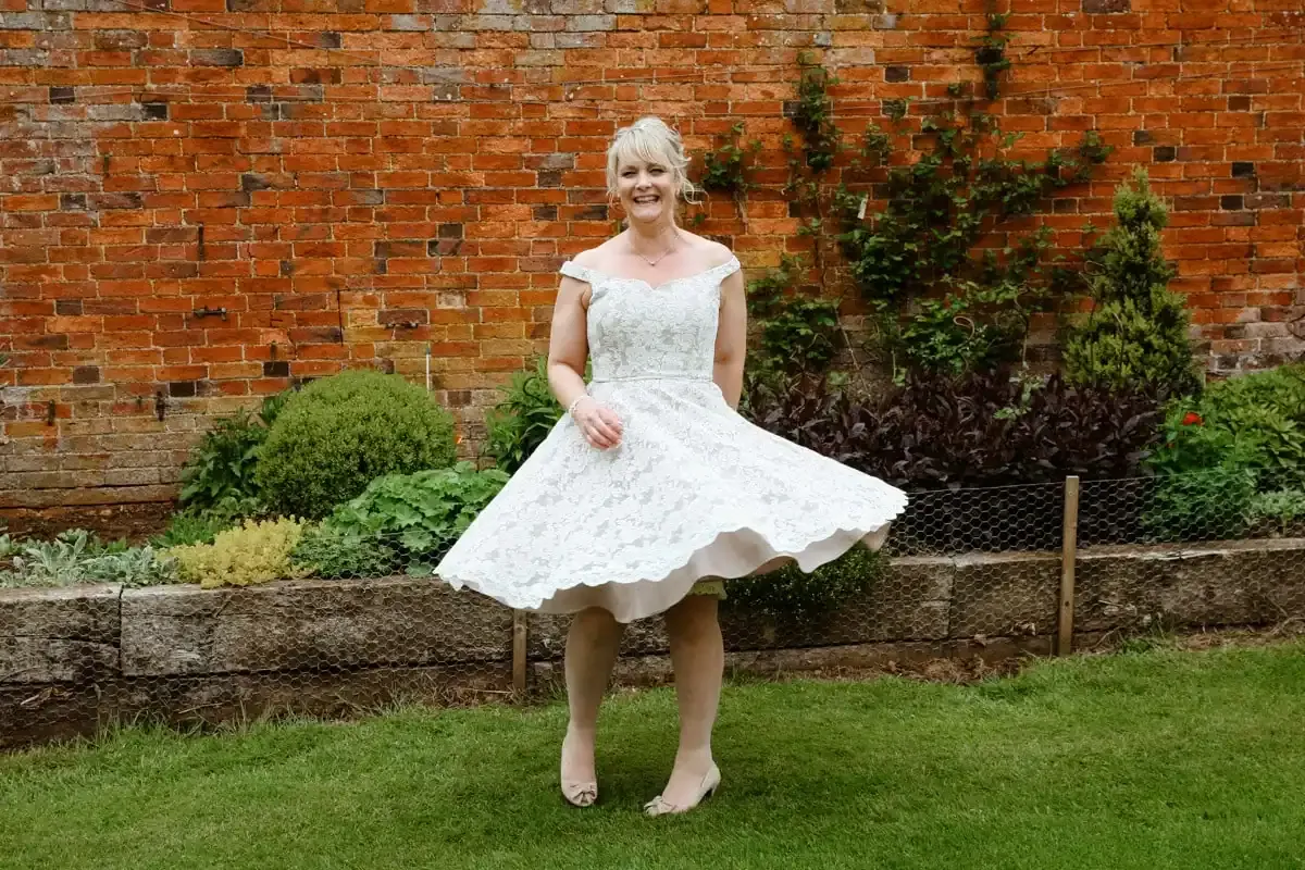 Smiling woman in white lace dress twirling in a garden.