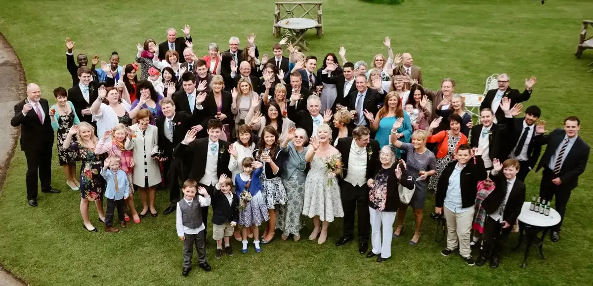 Wedding guests of all ages waving on a green lawn.