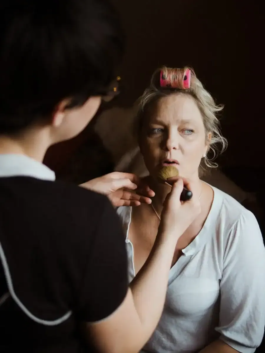 Blonde woman with pink rollers having makeup applied.