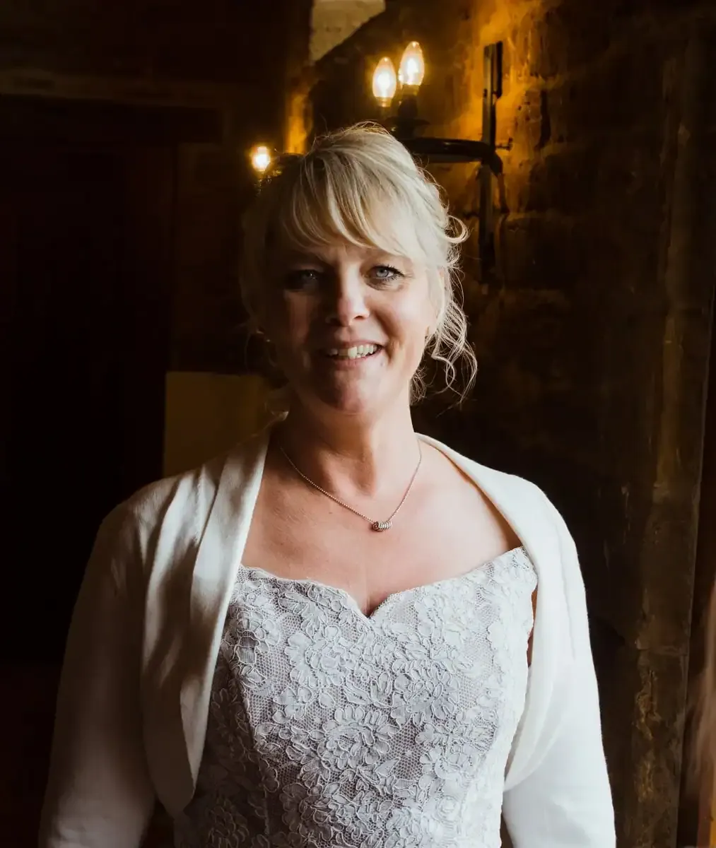 Smiling blonde woman in white lace dress and shrug.