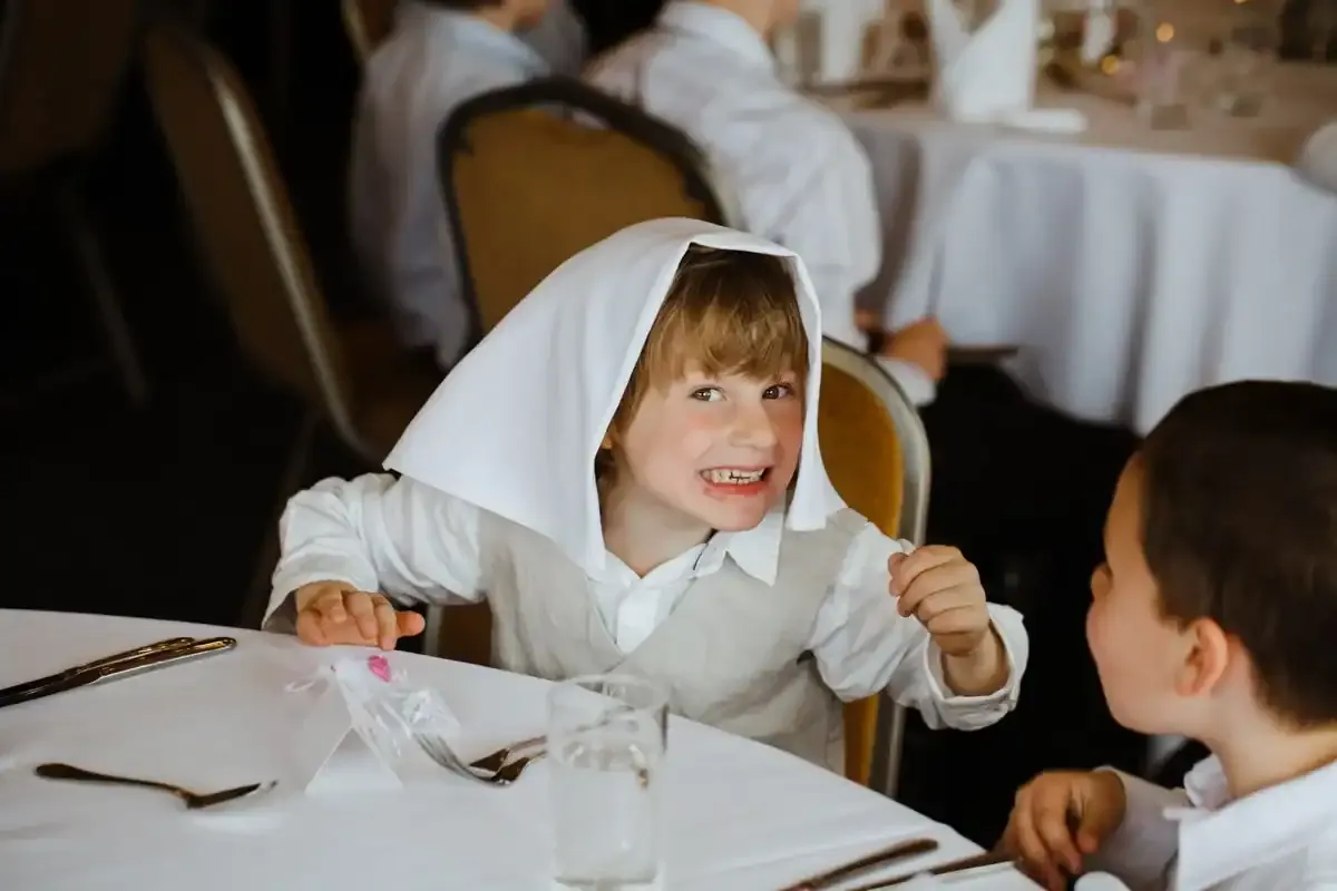 Blonde boy with white cloth on head makes a funny, toothy face.