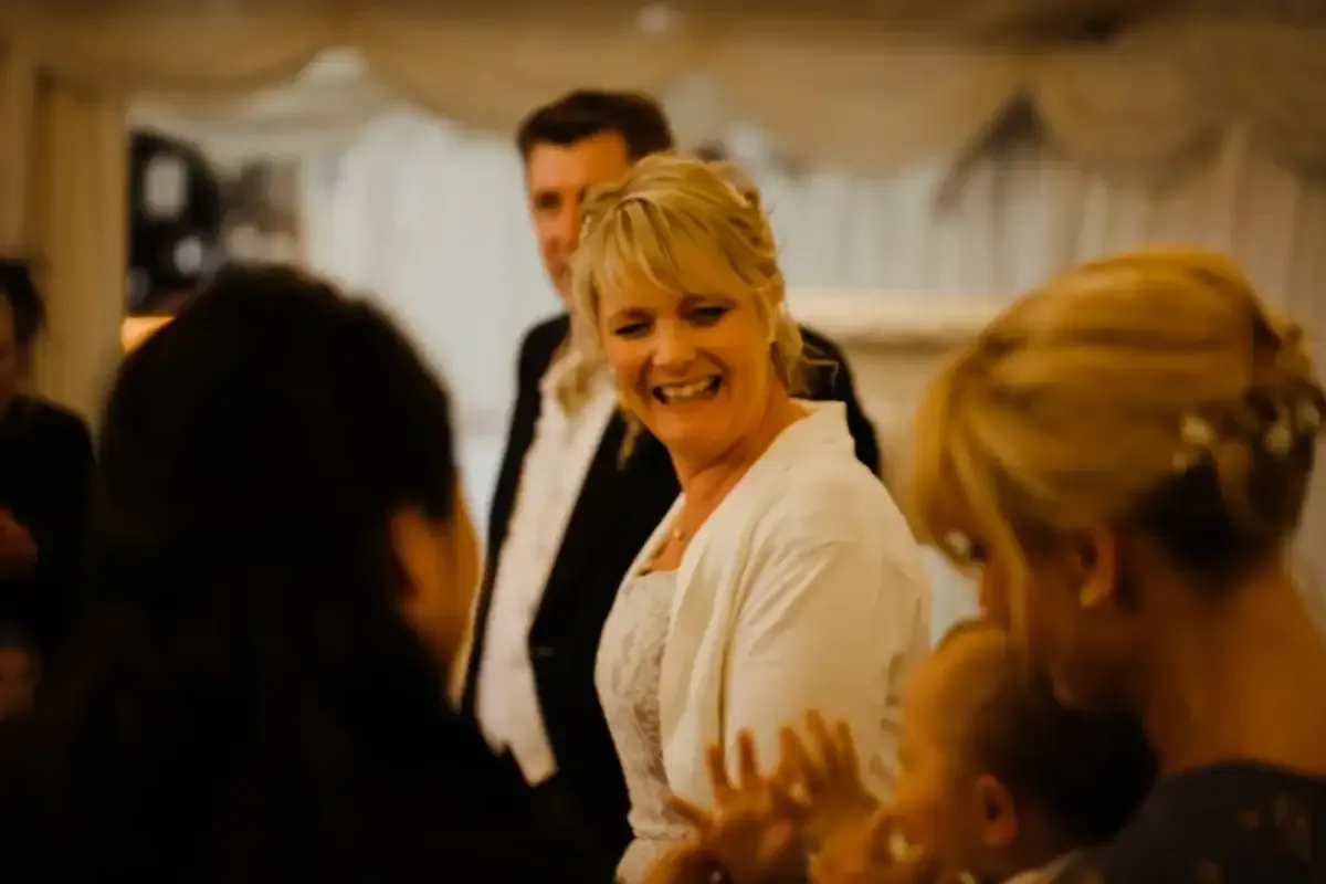 Laughing blonde woman in white dress, man and baby at a celebration.