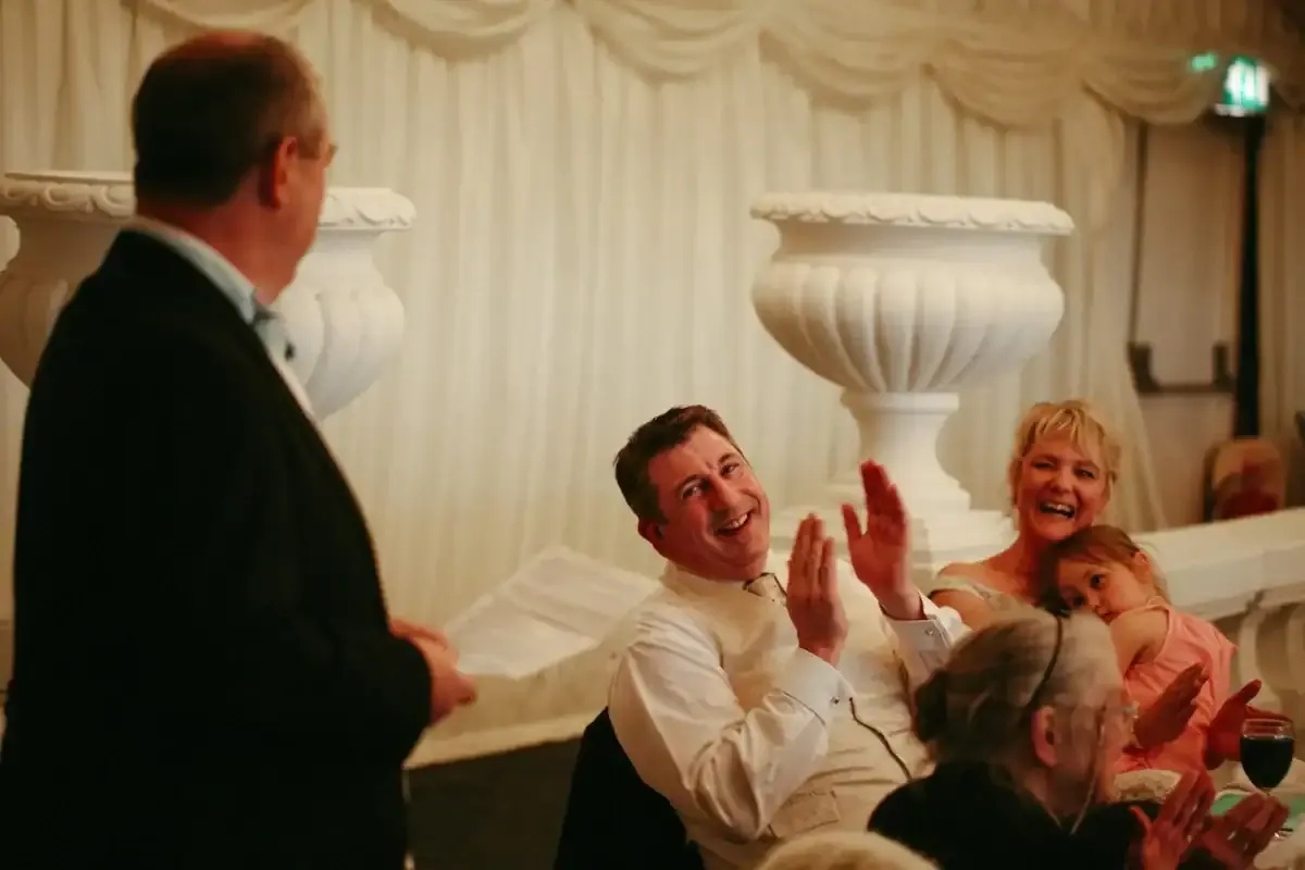People clapping and laughing at a speaker during a formal event.
