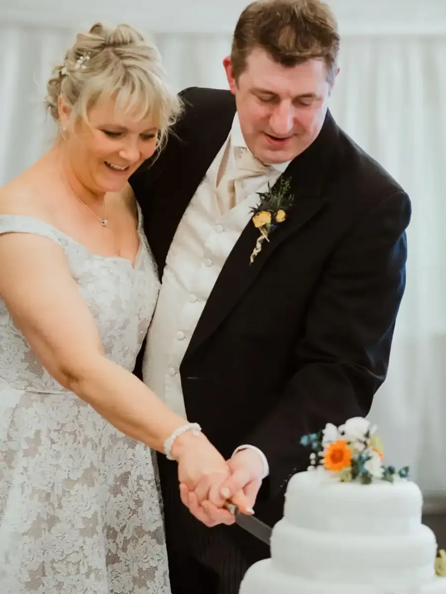 Smiling bride and groom cutting a white tiered wedding cake.