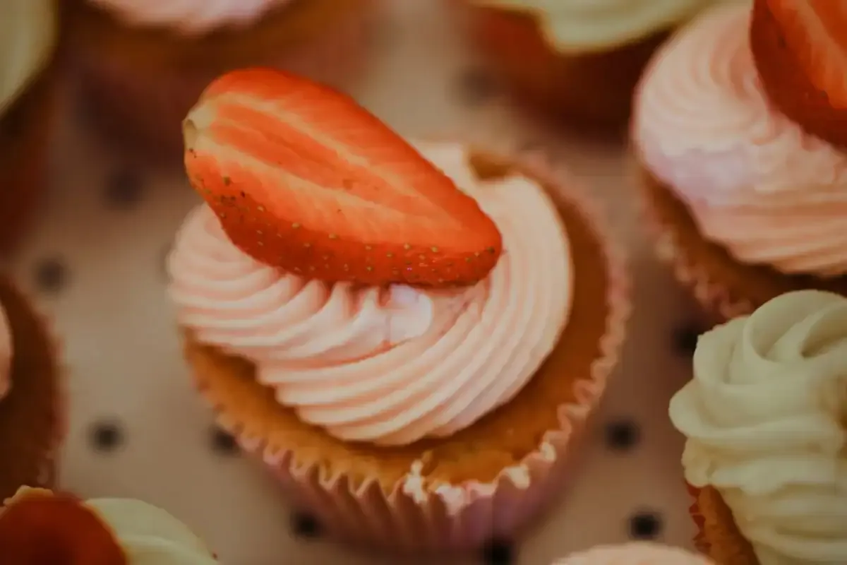 Several cupcakes with pink and white icing, some topped with strawberry halves.