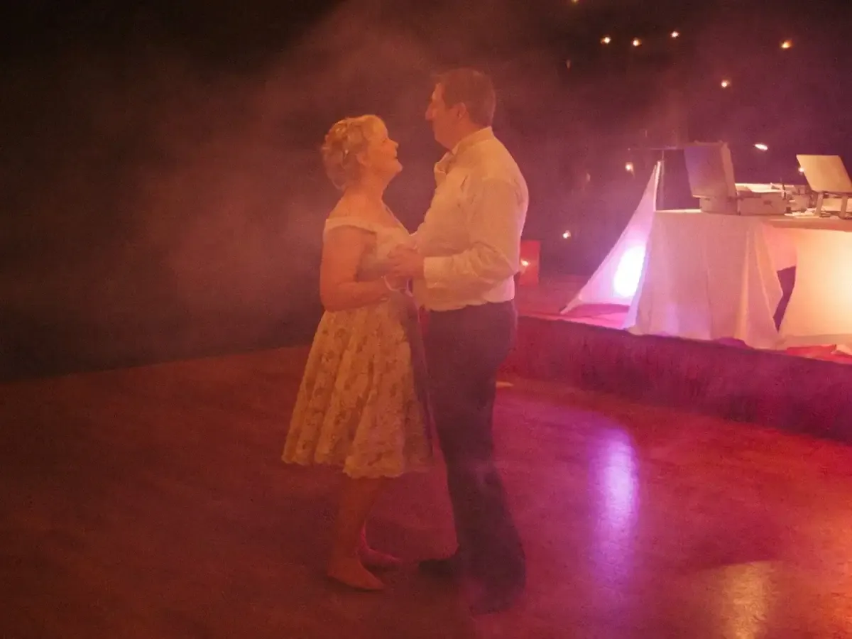 Man and woman dancing, looking at each other, under pink lights and smoke.