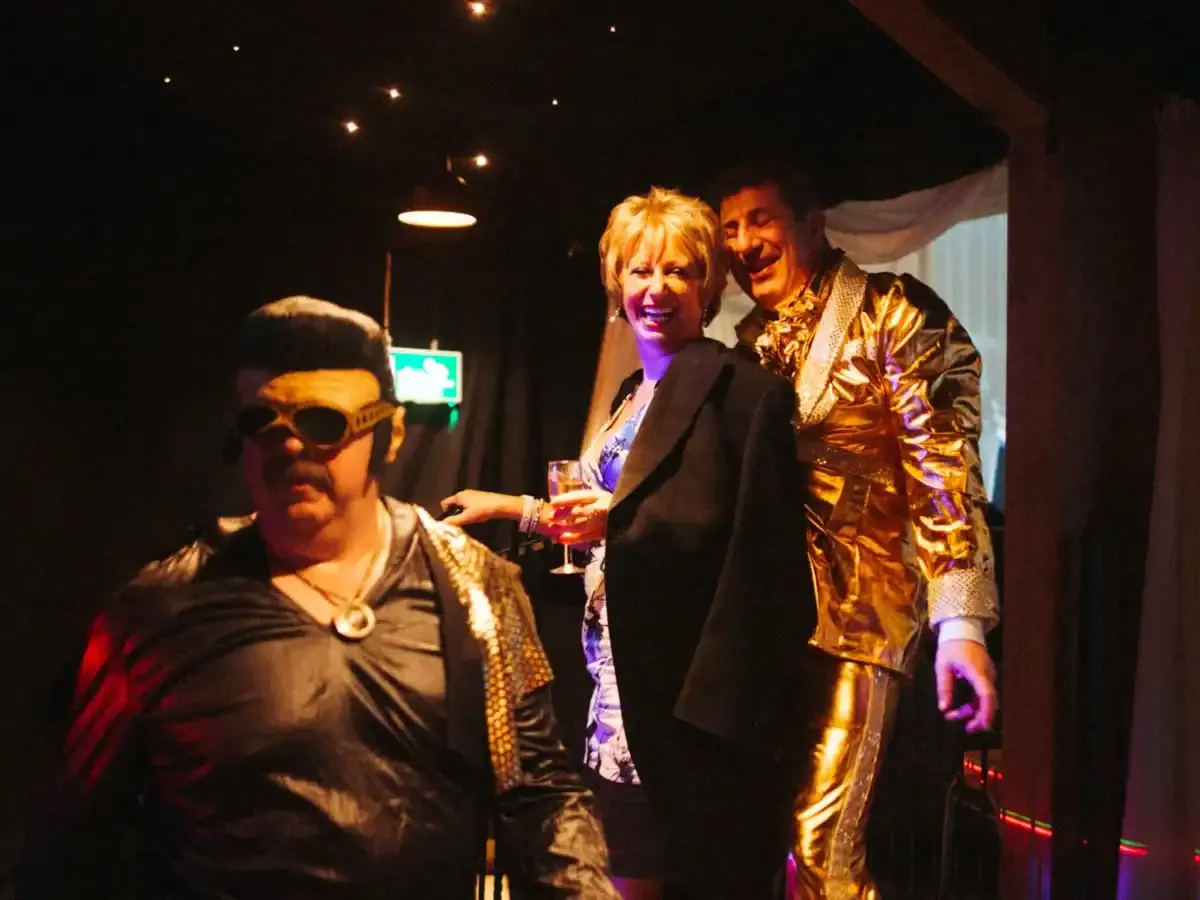 Elvis impersonator, smiling woman with drink, and man in gold suit.