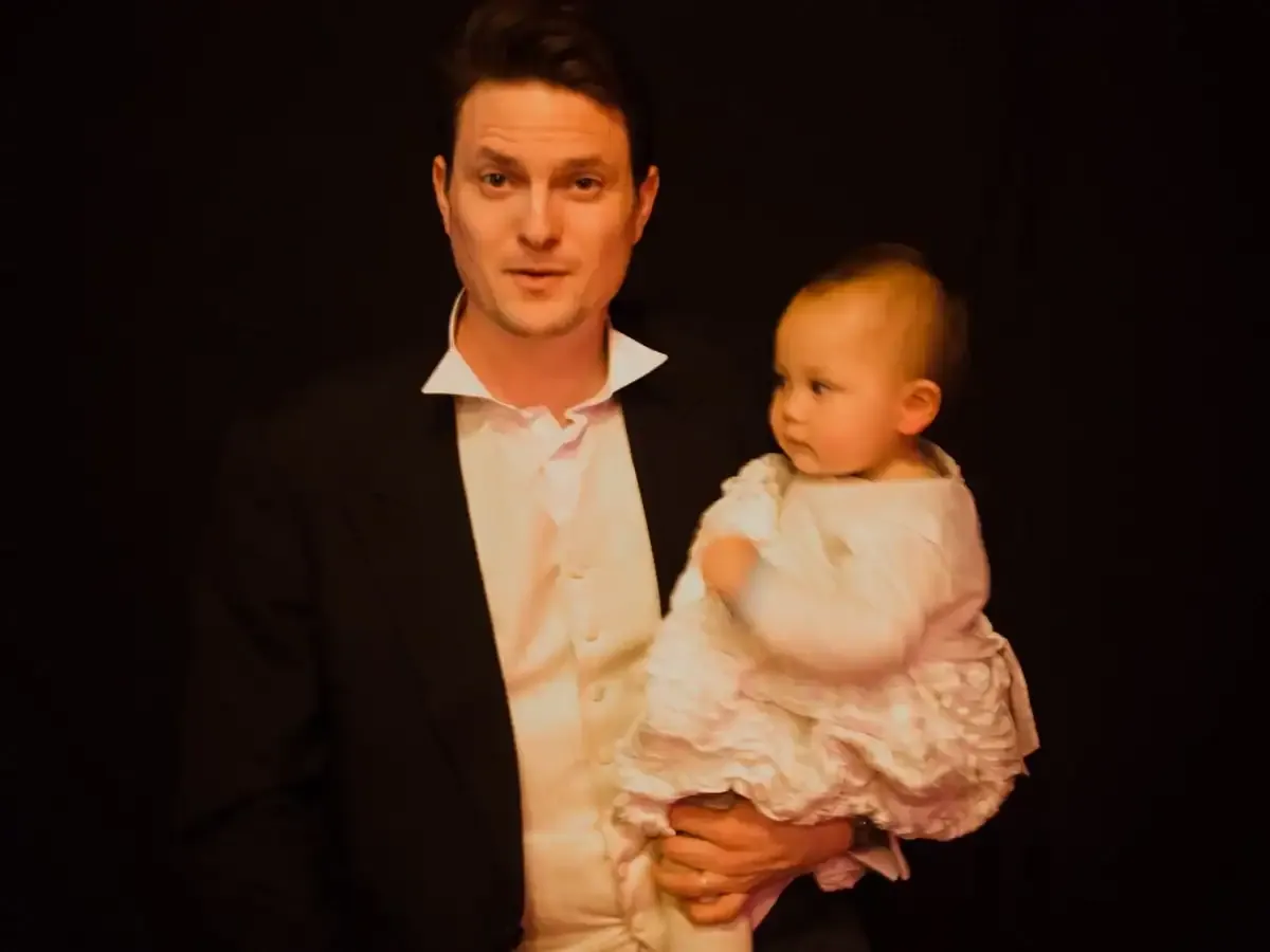Man in suit holds baby in white ruffled outfit.