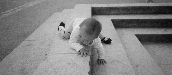 Black and white baby crawling on concrete surface near outdoor steps.