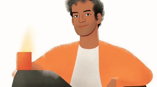 Smiling man in orange cardigan, next to a glowing orange candle.