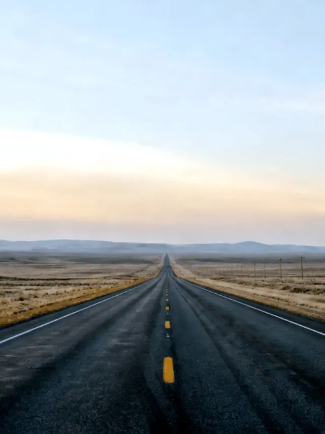 An empty highway running straight to a distant horizon at dawn, plains and low mountains on either side.
