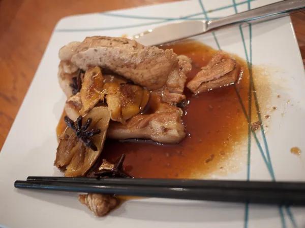 Cooked meat in brown sauce with ginger, star anise, chopsticks, knife on patterned plate.