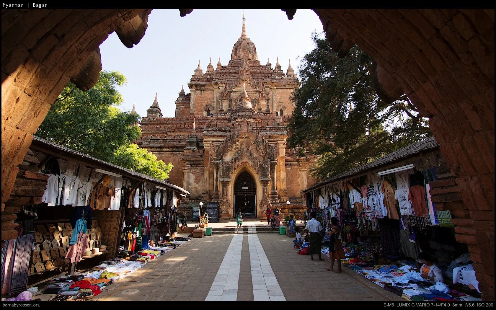 Ancient Bagan temple viewed through arches, flanked by market stalls.